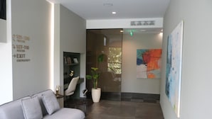 A modern lobby with a grey sofa, a bookshelf, a potted plant, and an abstract painting on the wall. - Boutique Hotel Adelar (Tirana)