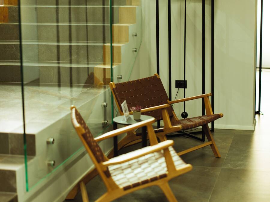 A modern interior with a glass staircase, wooden chairs, and a floor lamp.