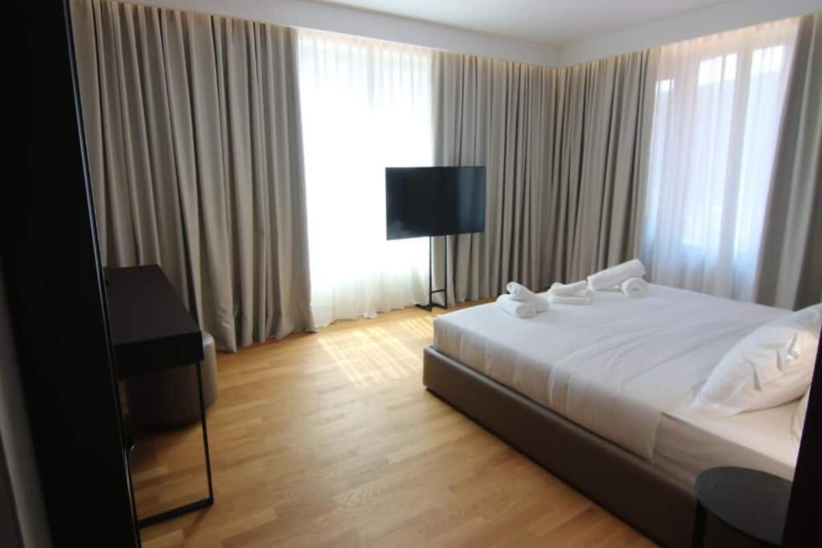 A hotel room with a large bed, a flat-screen TV mounted on the wall, and a wooden floor.