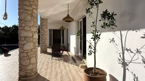 A spacious outdoor area with stone pillars, a wooden deck, a potted tree, and hanging lights.
