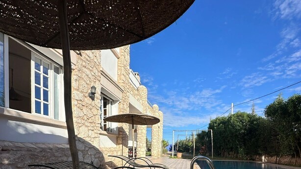 A poolside area with a stone building, lounge chairs, and a clear blue sky.