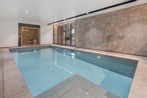 An indoor swimming pool with a tiled floor, a wooden door, and a large glass window.