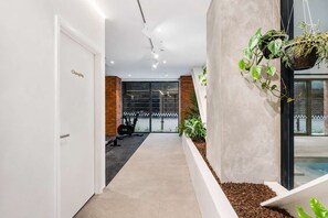 Un couloir avec une porte portant l’inscription « Vestiaires », un mur de briques, une fenêtre donnant sur un paysage et une plante suspendue.