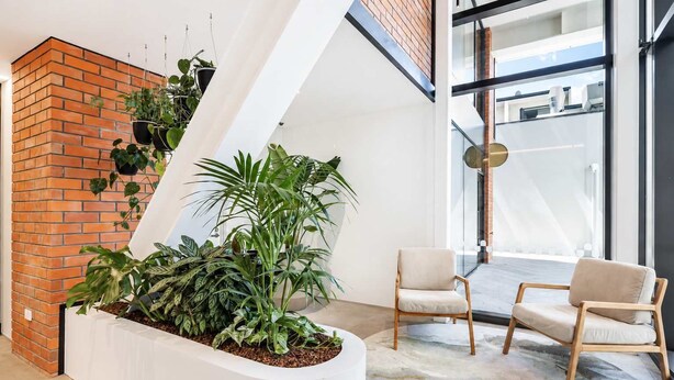 A modern interior with a brick wall, a white planter with plants, and two chairs.
