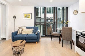 A modern living room with a blue sofa, a round coffee table, and a dining area with a chair and table.