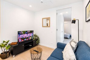 A modern living room with a flat-screen TV, a sofa, a coffee table, and a potted plant.