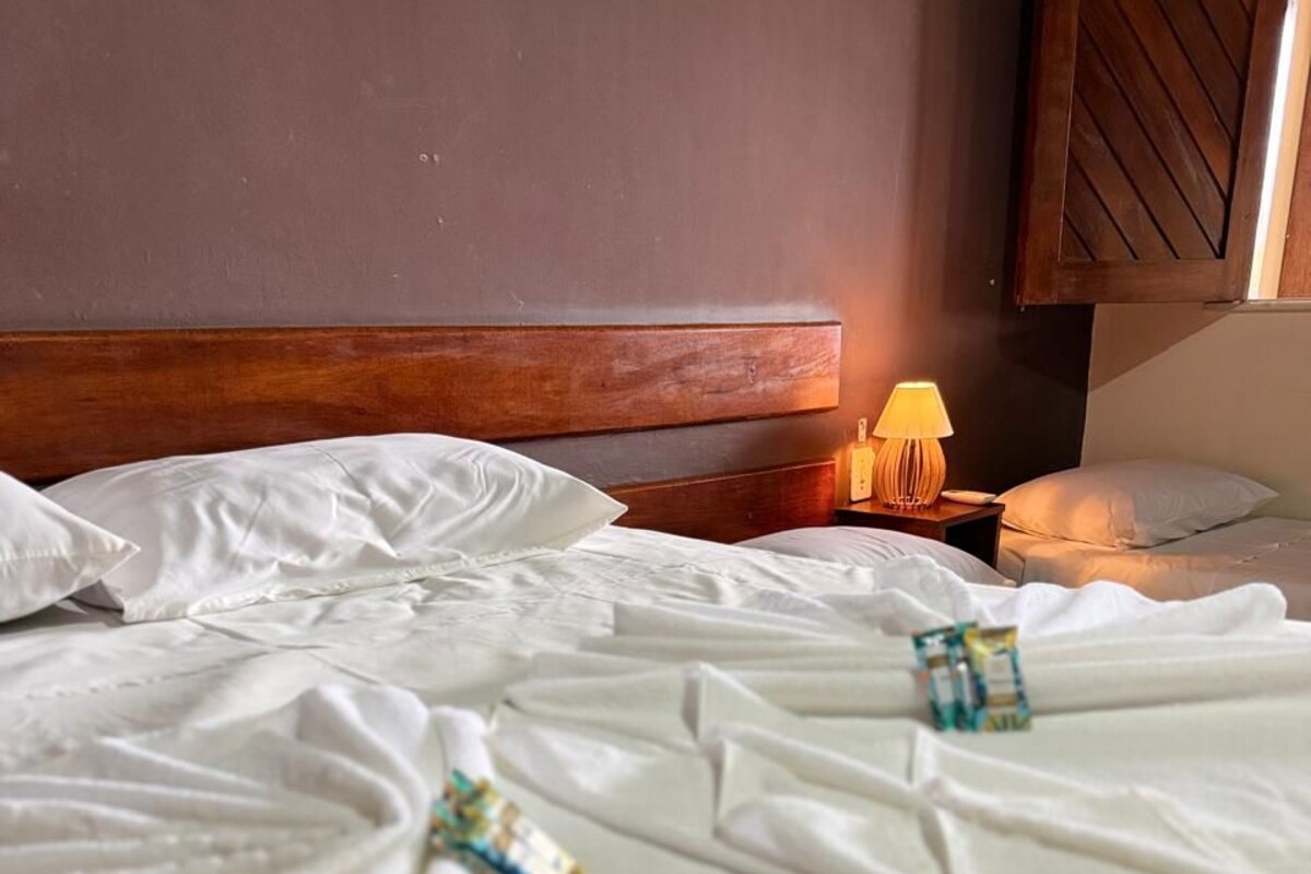A hotel room with a wooden headboard, a bedside table with a lamp, and neatly made beds.
