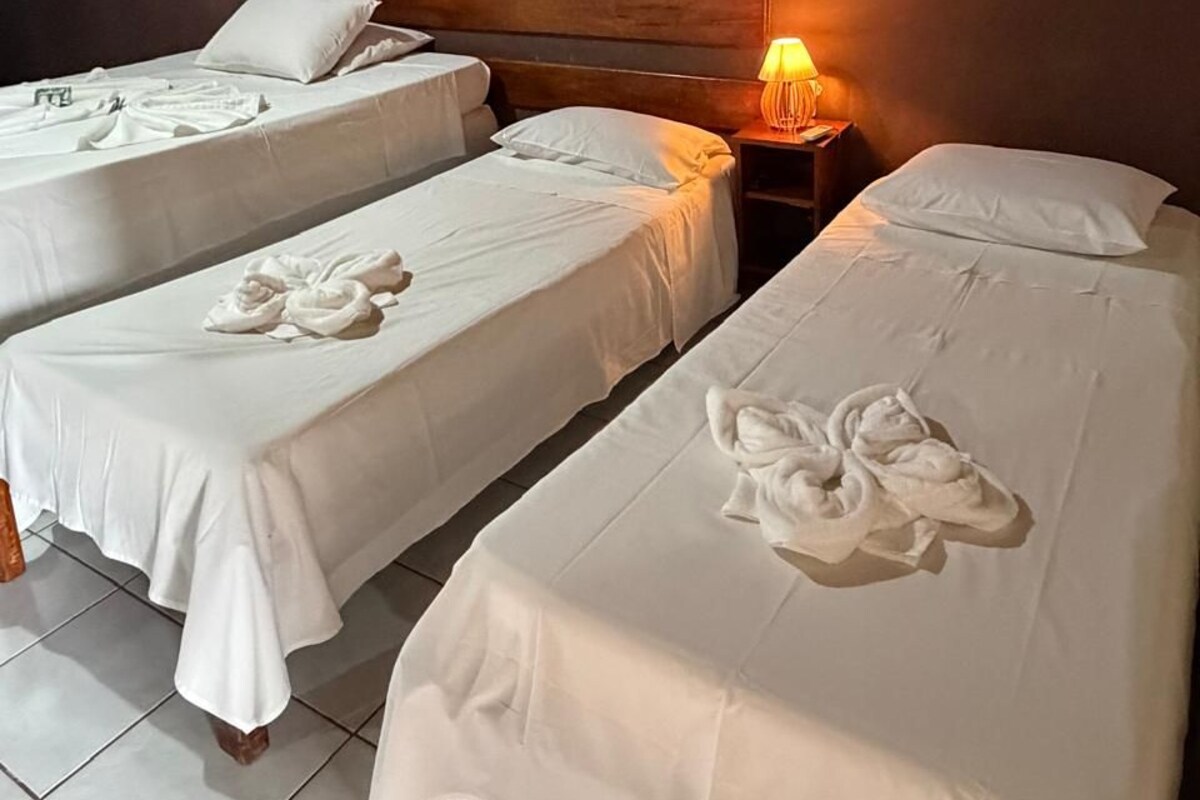 A hotel room with two single beds, a wooden headboard, a nightstand with a lamp, and towels neatly arranged on the beds.