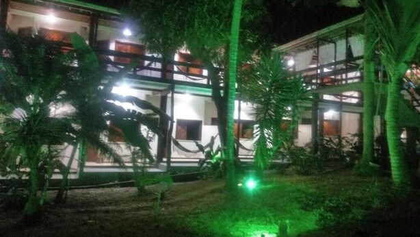 A building with multiple balconies, surrounded by palm trees and a well-lit garden area. - POUSADA PORTAL DO SOL  (Itacaré)