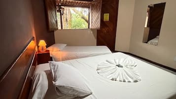 A hotel room with two beds, a nightstand with a lamp, a window with curtains, and a wooden ceiling.