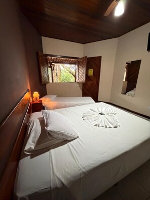 A hotel room with two beds, a nightstand with a lamp, a window with curtains, and a wooden ceiling. - POUSADA PORTAL DO SOL  (Itacaré)