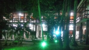 A building with multiple floors, surrounded by trees and illuminated by green lights. - POUSADA PORTAL DO SOL  (Itacaré)