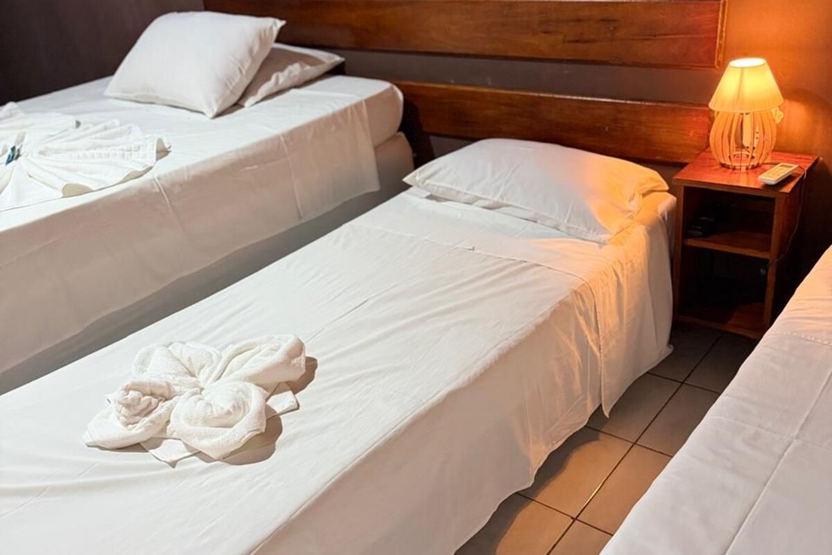 A hotel room with two beds, a wooden headboard, a nightstand with a lamp, and towels on the beds.