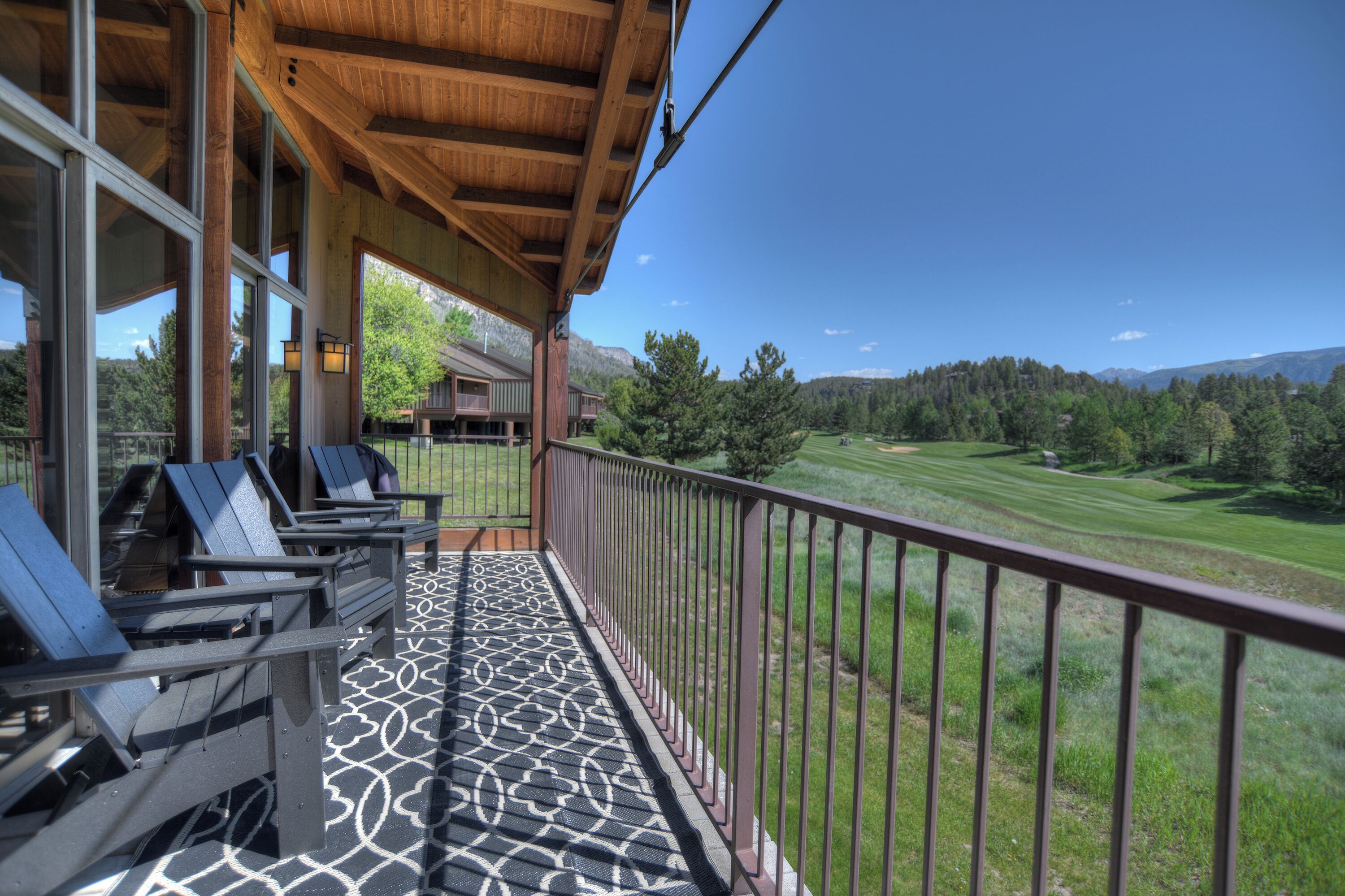 A balcony with outdoor seating, a view of a golf course, and a mountain backdrop.