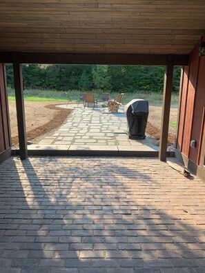 A covered patio area with a brick floor, outdoor seating with chairs and a table, and a barbecue grill.