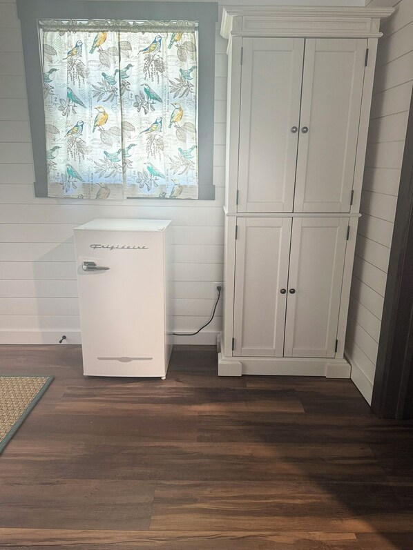 A kitchen with a white refrigerator, a window with a bird pattern curtain, and a white cabinet.