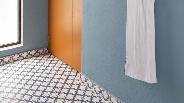 A room with a wooden door, a white robe hanging on the wall, and patterned floor tiles.