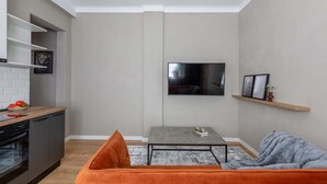 A compact living space with a kitchen, a grey sofa, a coffee table, and a flat-screen TV mounted on the wall. - Holt Rossetti Residences Exclusive Urban Lofts (Bucharest)