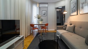 A modern living room with a flat-screen TV, a glass coffee table, a sofa, and a dining area with chairs and a table. - Holt Rossetti Residences Exclusive Urban Lofts (Bucharest)