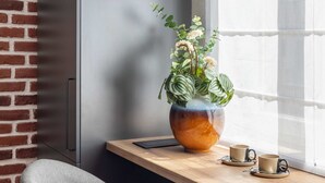 A corner of a room with a brick wall, a wooden table, a grey chair, a potted plant, and two cups. - Holt Rossetti Residences Exclusive Urban Lofts (Bucharest)