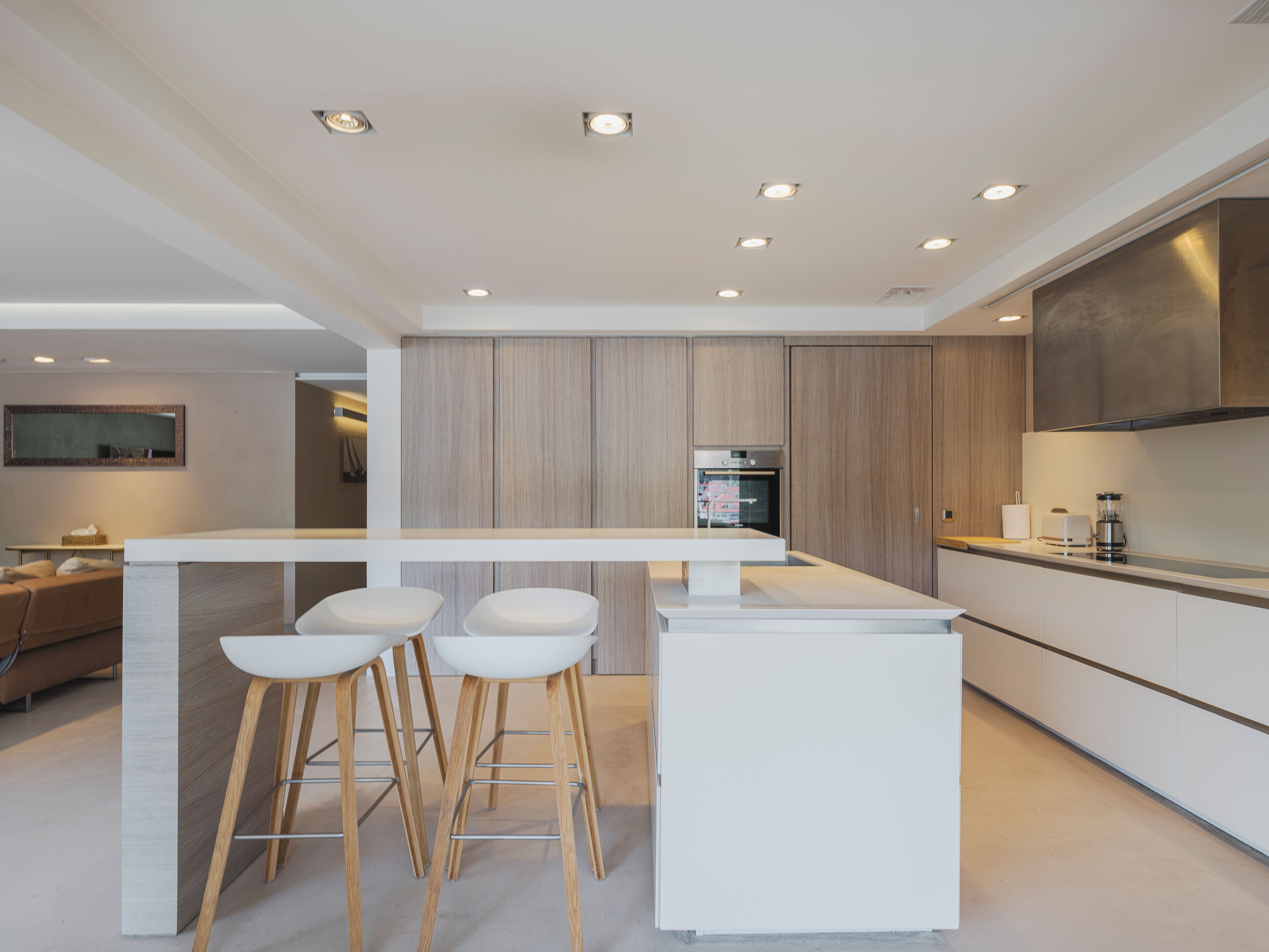 A modern kitchen with a central island, bar stools, wooden cabinets, and built-in appliances.