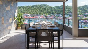 A dining area with a table set for four, overlooking a marina and a hillside town. - Beautiful 2-bedroom apartment in Gustavia with harbor view in Saint Barthélémy (Gustavia)
