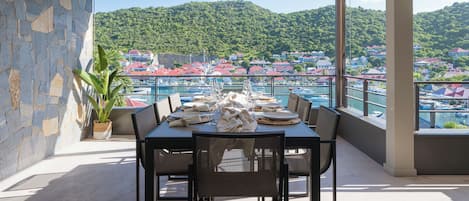 A dining area with a table set for four, overlooking a marina and a hillside town.
