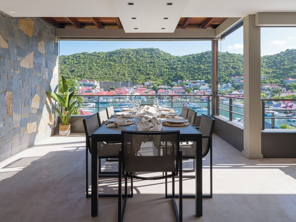 A dining area with a table set for four, overlooking a marina and a hillside town.