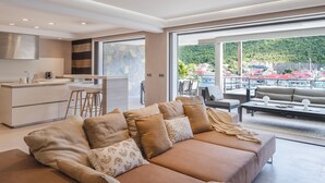 A modern living room with a large sofa, a dining area, and a view of a coastal town. - Beautiful 2-bedroom apartment in Gustavia with harbor view in Saint Barthélémy (Gustavia)