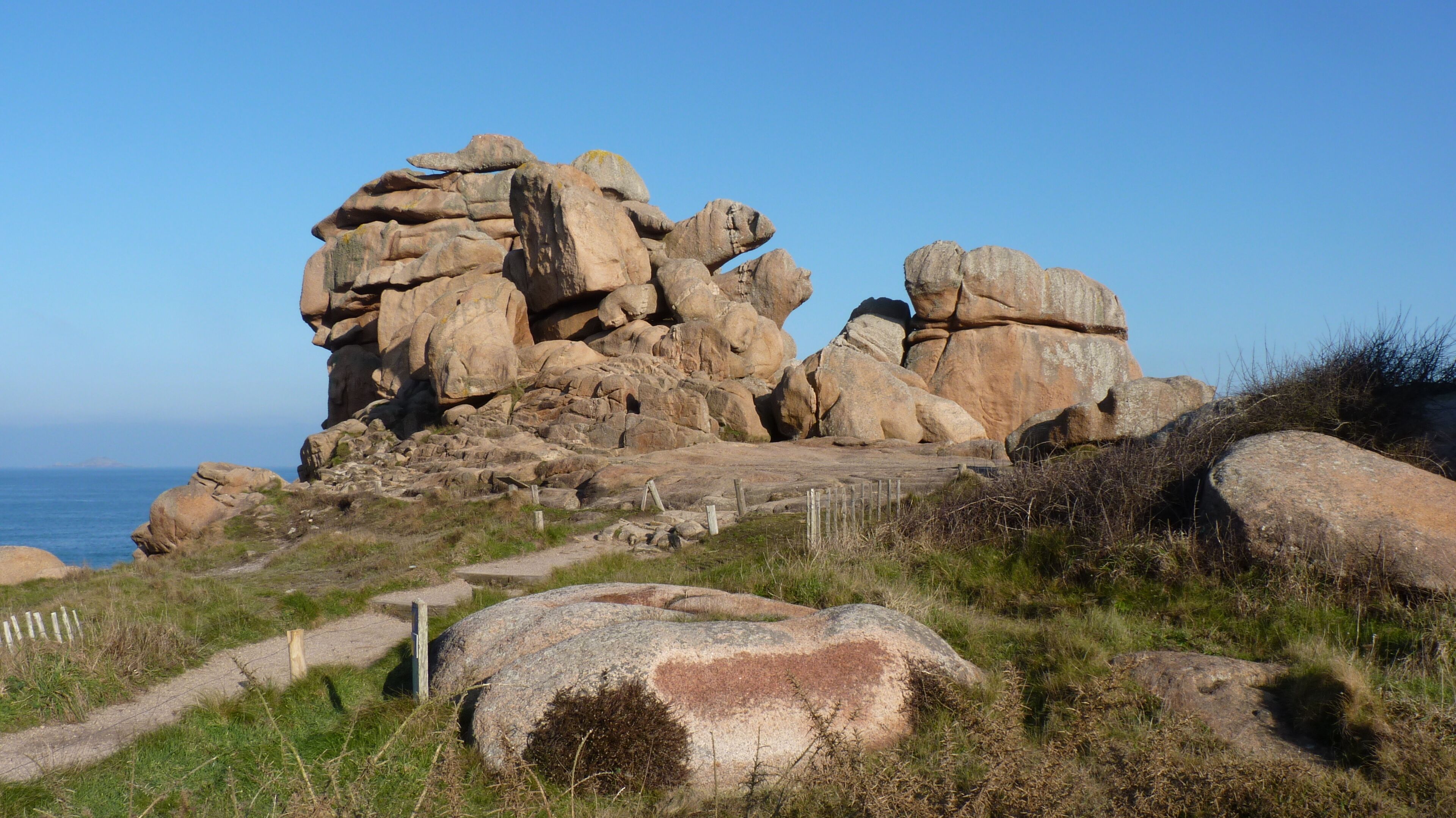Un paysage côtier rocheux, avec de gros blocs de pierre et un ciel dégagé.