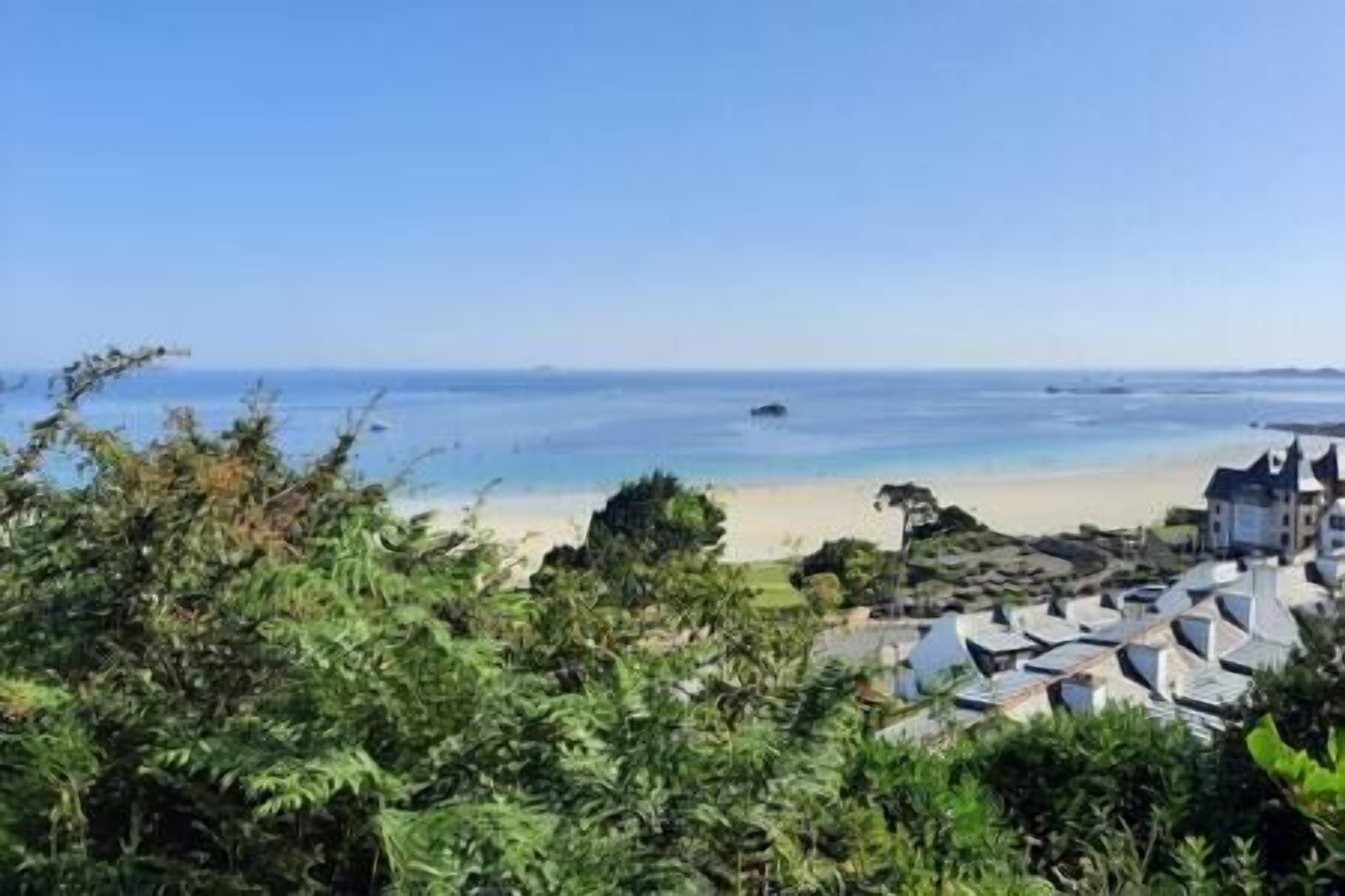 A coastal view with a beach, clear sky, and buildings with a uniform architectural style.