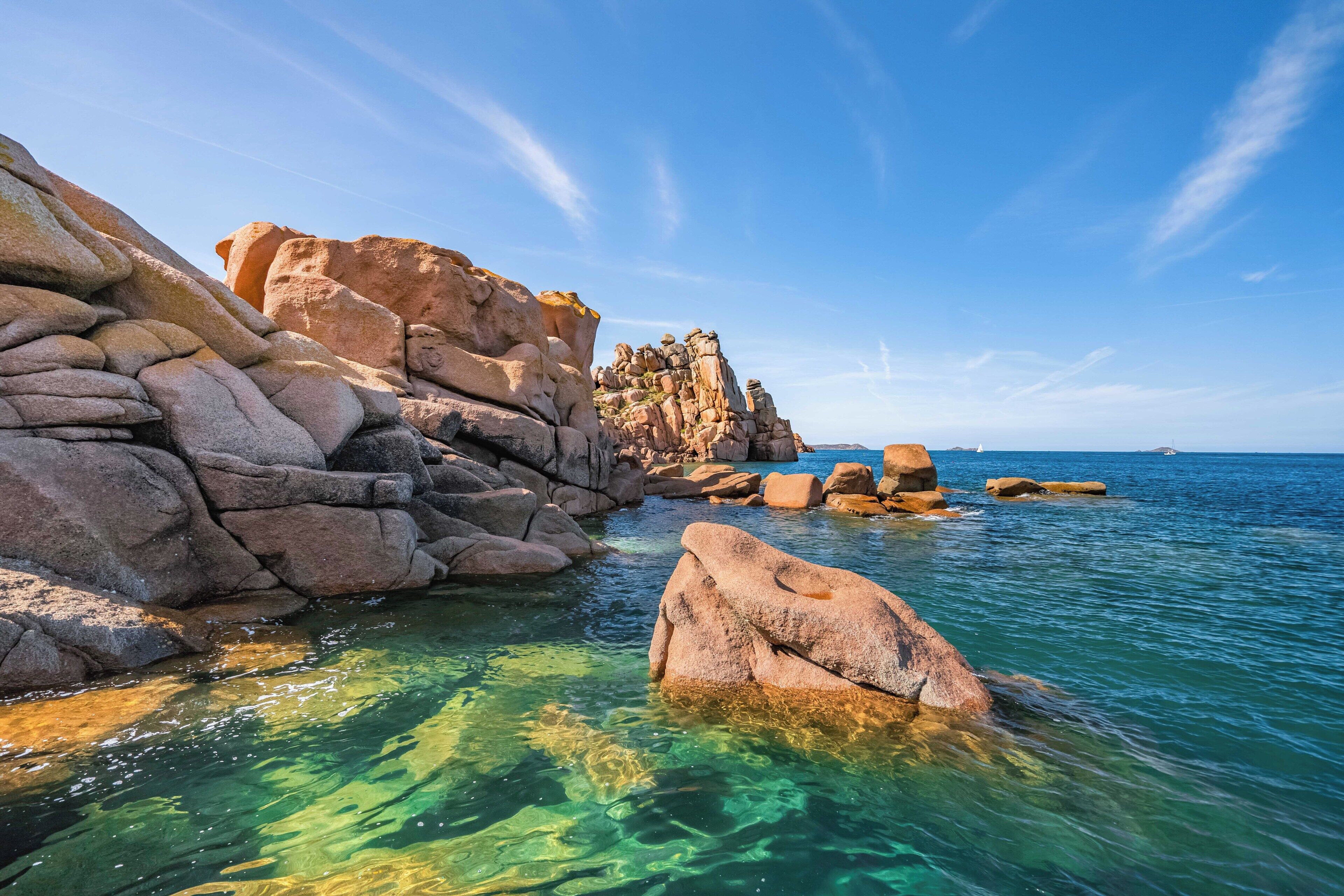 A coastal landscape with clear water, large rocks, and a distant view of the sea.