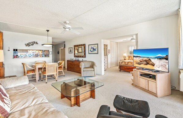 A spacious living room with a glass coffee table, a sofa, a TV, and a dining area with chairs and a table.