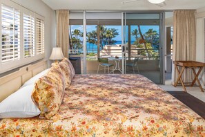 A hotel room with a large bed, a balcony with a view of the ocean, and a small table with chairs.