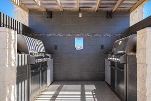 Un área de cocina al aire libre con dos parrillas de barbacoa, un salpicadero de azulejos y una pequeña ventana.
