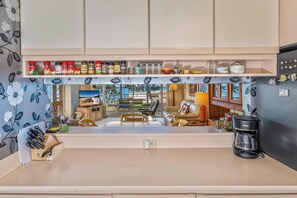 Una cocina con vista al área de estar, una cafetera y varios utensilios de cocina sobre la encimera.