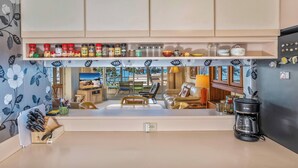 A kitchen with a view of the living area, a coffee maker, and various kitchen items on the counter. - Kamaole Beach Royale #312 3nd Flr, Ocean View, Steps from Beach, Full Kitchen (Kihei)