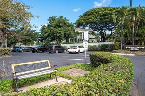 A parking area with a bench, a sign for 'KAMJAME BEACH ROYALE', and a building in the background.