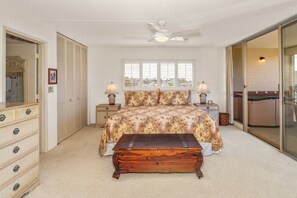 A bedroom with a bed, bedside lamps, a wooden chest, a dresser, and a sliding glass door leading to a balcony.