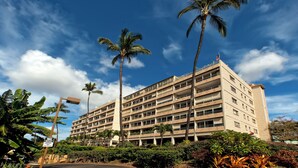 A multi-story hotel with a flat facade, surrounded by palm trees and lush greenery. - Kamaole Beach Royale #312 3nd Flr, Ocean View, Steps from Beach, Full Kitchen (Kihei)