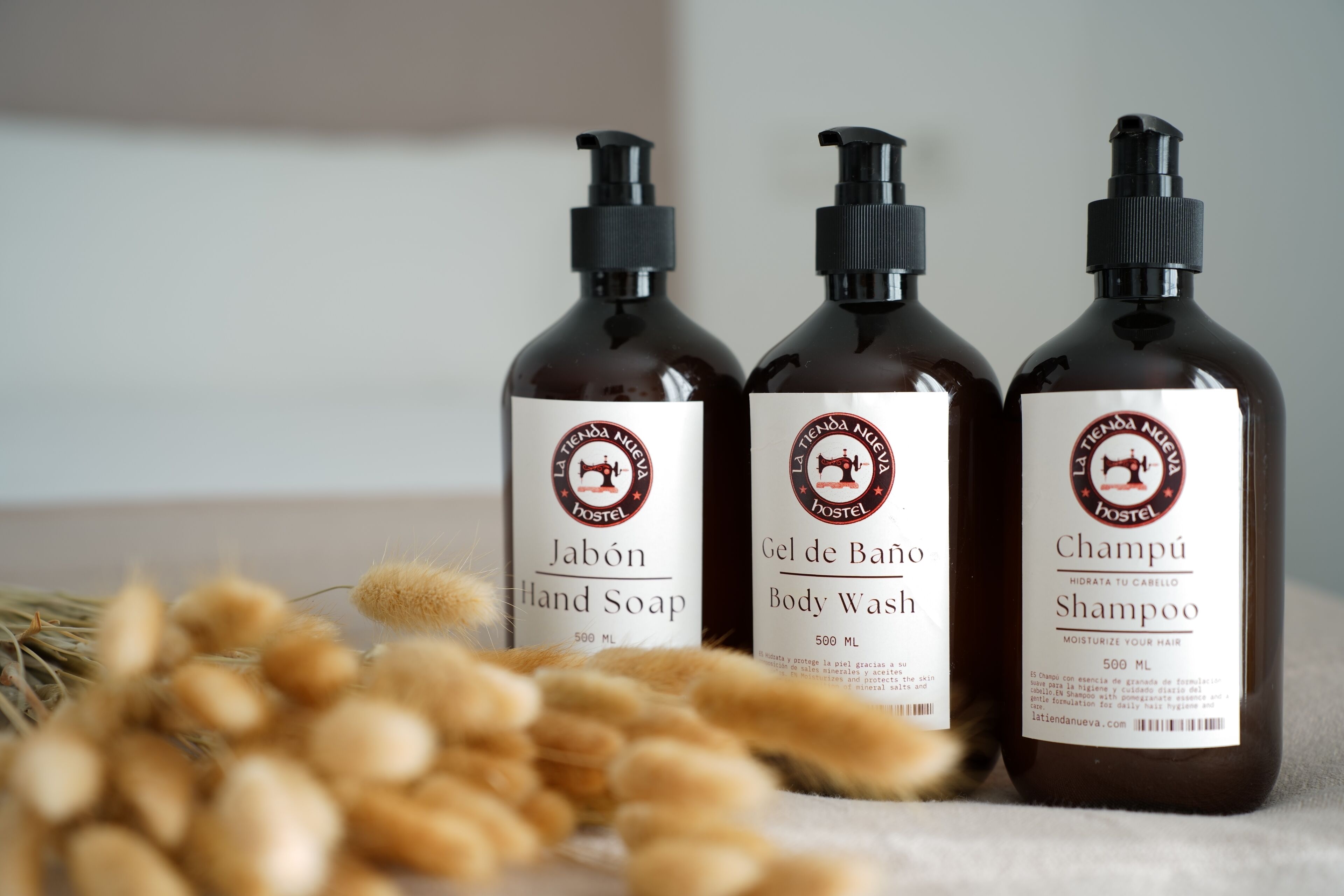Three bottles of La Tienda Nuda Hostel personal care products: hand soap, body wash, and shampoo.