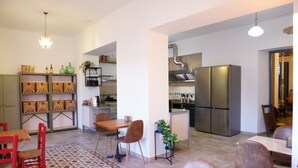 A modern kitchen with a stainless steel refrigerator, a dining area with a wooden table and chairs, and a patterned rug on the floor. - La Tienda Nueva (Còmpeta)