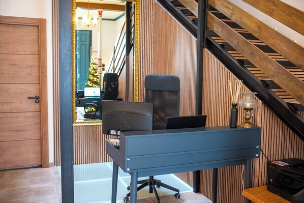 Un bureau à domicile avec un bureau, une chaise et un ordinateur. Un miroir reflète un escalier et un sapin de Noël.