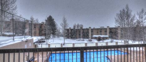 Zona exterior cubierta de nieve con piscina, rodeada de una valla y edificios al fondo.