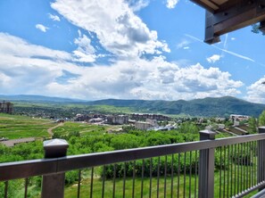 Een balkon met uitzicht op een stad, groene velden en bergen.