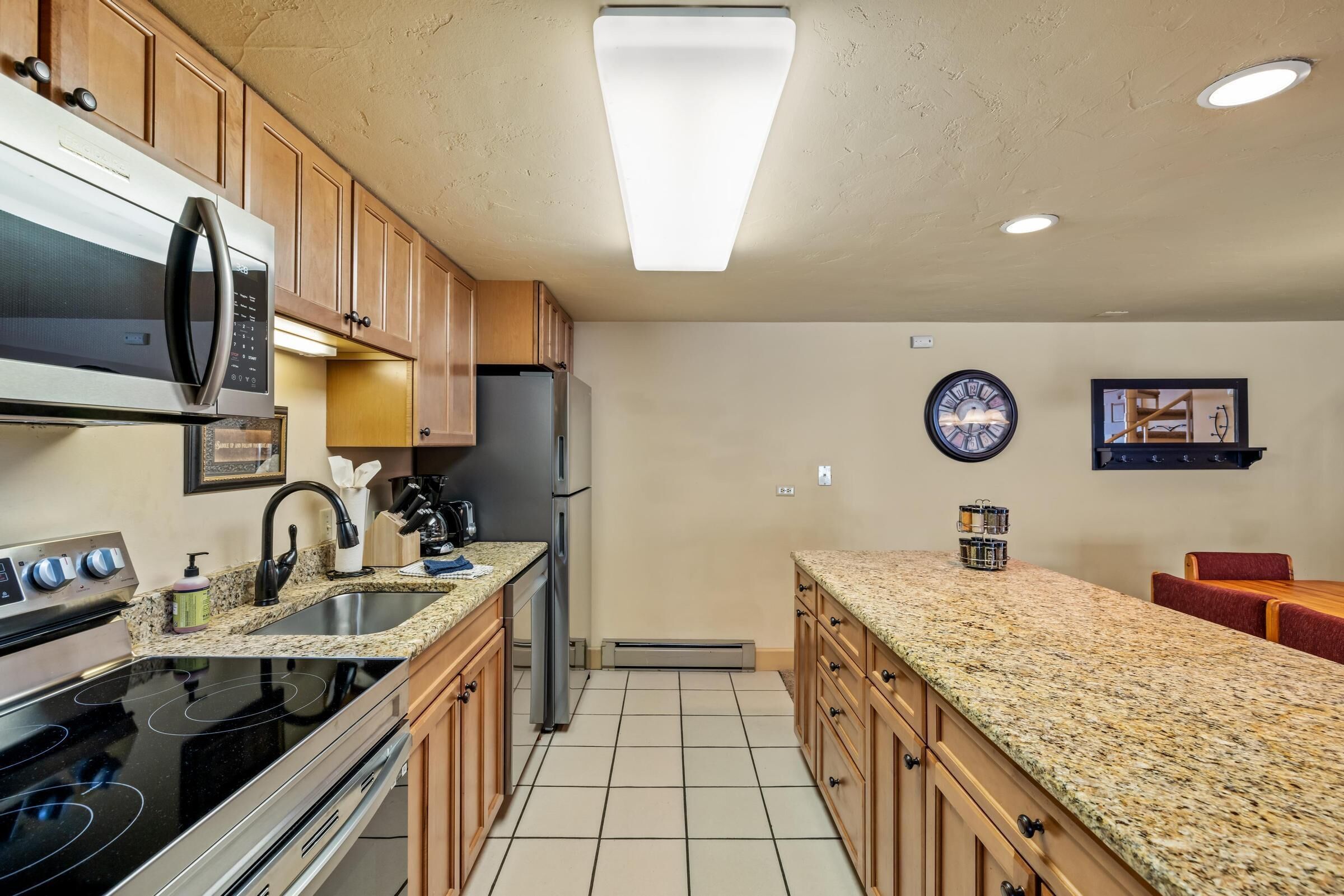 A modern kitchen with granite countertops, stainless steel appliances, wooden cabinets, and a central island.
