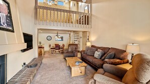 A spacious living room with a high ceiling, a wooden coffee table, a brown leather sofa, and a TV mounted on the wall. - 2 Level Unit w/ Pool Hot Tubs Private Deck (Steamboat Springs)
