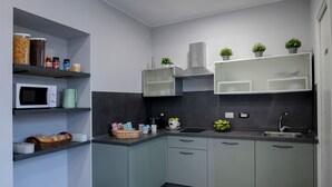 A modern kitchen with a microwave, coffee maker, and various kitchen appliances. There are shelves with jars and a basket of bread. - DoppioSei -Guest House (Rome)
