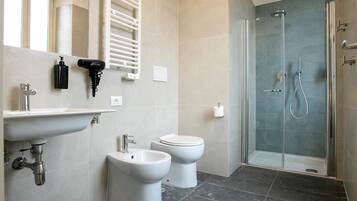 Un baño moderno con lavabo, bidé, inodoro y ducha con mampara de vidrio.