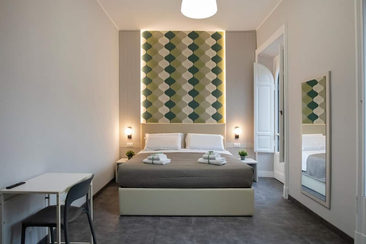 Ein modernes Hotelzimmer mit einem großen Bett, Nachttischen, einem Schreibtisch und einem Sessel.